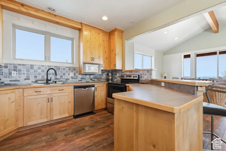 Kitchen featuring natural wood cabinetry, patterned tile backsplash, stainless steel appliances, wood-finish flooring, and a peninsula with a stone-top counter