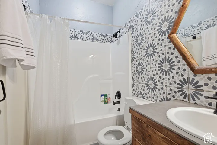 Bathroom featuring patterned wall tile, vanity with wood-finish cabinetry, neutral countertop, and matte black plumbing fixtures