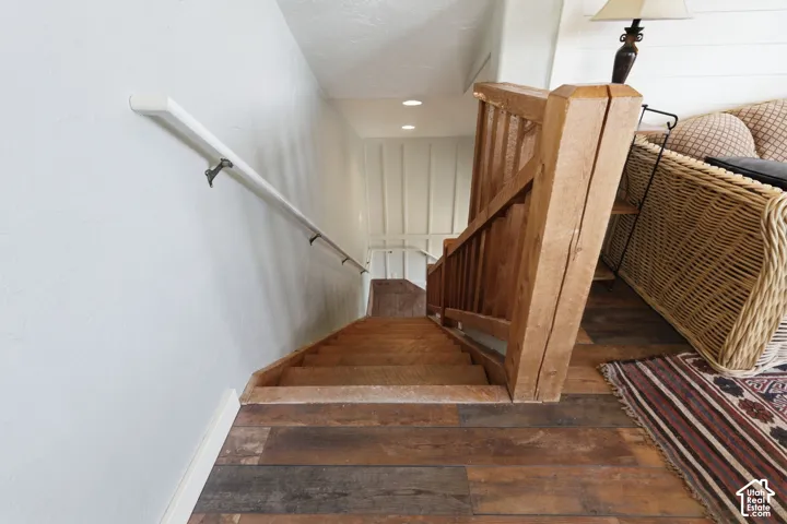 Staircase featuring wood-finish flooring, custom wood newel post and balusters, white handrail, and recessed lighting
