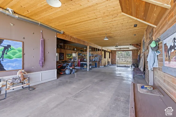 Spacious outbuilding featuring a concrete floor, vaulted wood-plank ceiling, exposed beam construction, and integrated overhead lighting