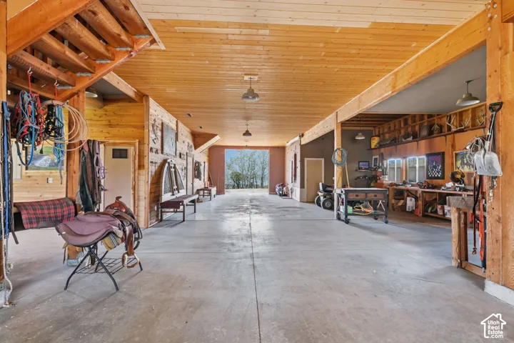 Expansive outbuilding featuring exposed wood-beam construction, tongue-and-groove wood ceilings, concrete flooring, built-in wooden shelving, and industrial-style pendant lighting
