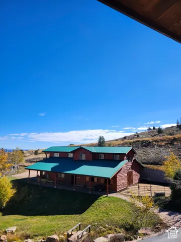 Multi-level wood-sided structure featuring a standing seam metal roof, expansive covered porch, and attached paddock enclosure