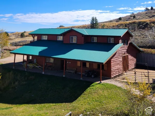 Log-style structure with a green metal roof, wrap-around covered porch, and exterior fenced enclosure