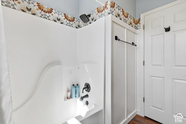 Bathtub and shower surround featuring geometric patterned tile accents, matte black plumbing fixtures, board and batten wall paneling, and a six-panel door