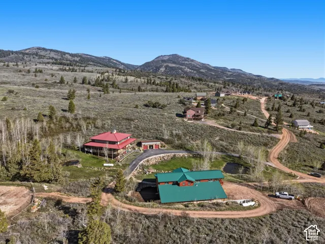 Aerial perspective featuring multi-structure property with metal roofing, extensive acreage, paved driveway, and mountain terrain backdrop