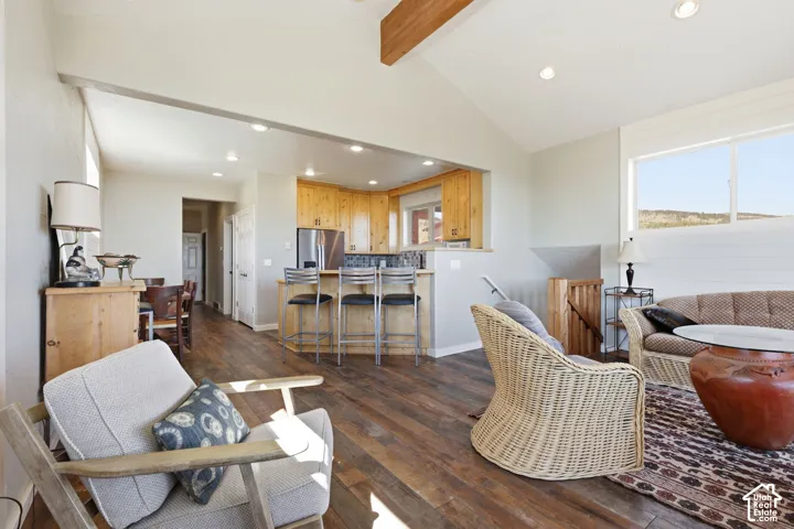 Vaulted ceilings with exposed timber beams, wood-finish flooring, recessed lighting, and kitchen featuring wood cabinetry and an integrated breakfast bar