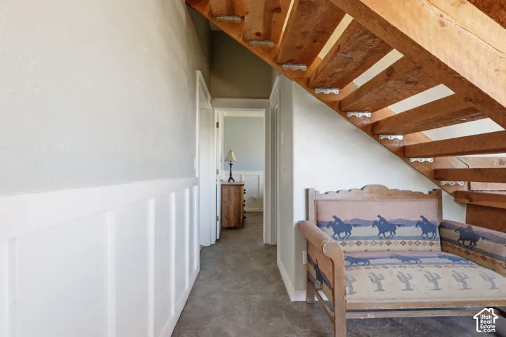 Open-riser wood staircase featuring exposed structural timber beams, complemented by white wainscoting and smooth wall finishes