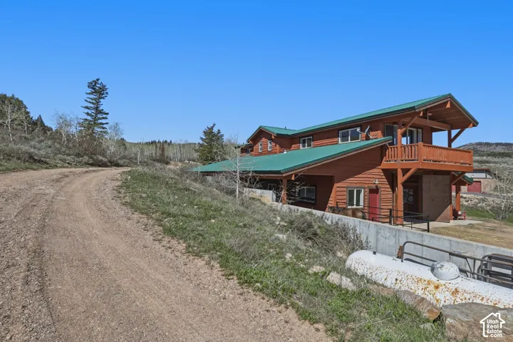 Multi-story log-style exterior featuring a green metal roof, wrap-around upper balcony, and structural timber framing