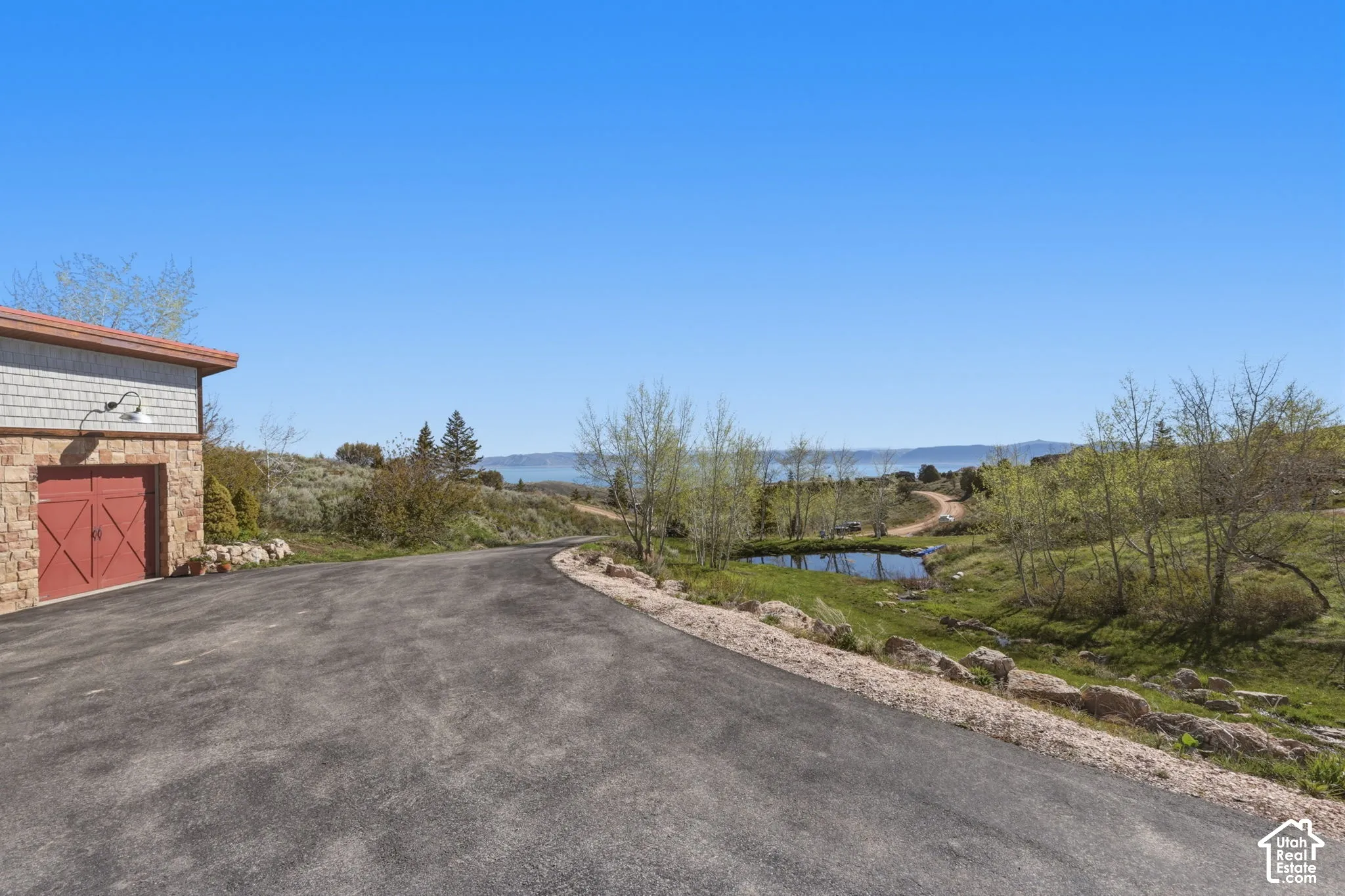 Asphalt driveway with stone foundation garage, including wood-style garage doors, exterior wall-mounted lighting, and natural pond