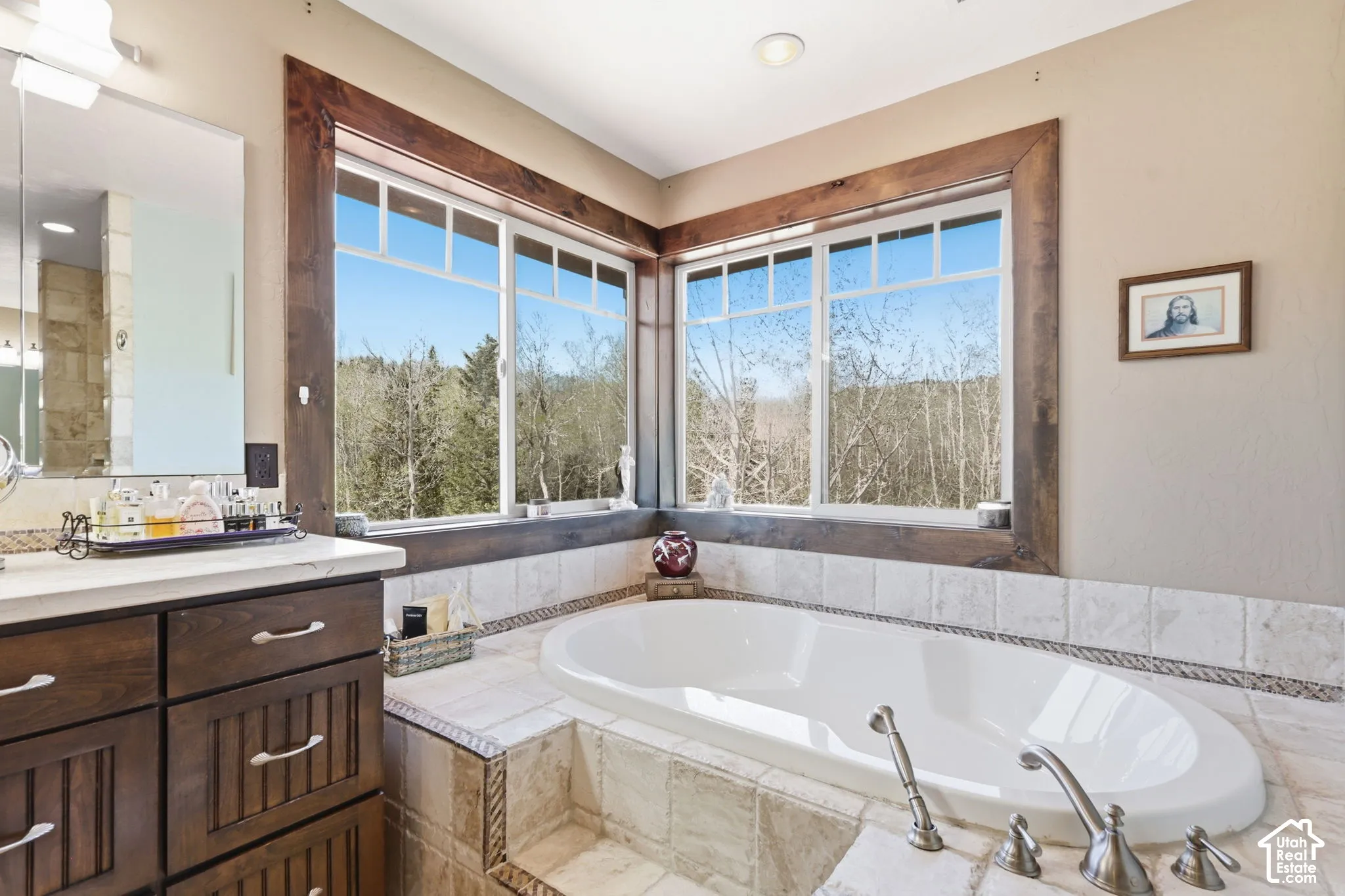 Built-in soaking tub with a tiled surround, custom wood window trim, dual-pane corner windows, and wood-finish cabinetry
