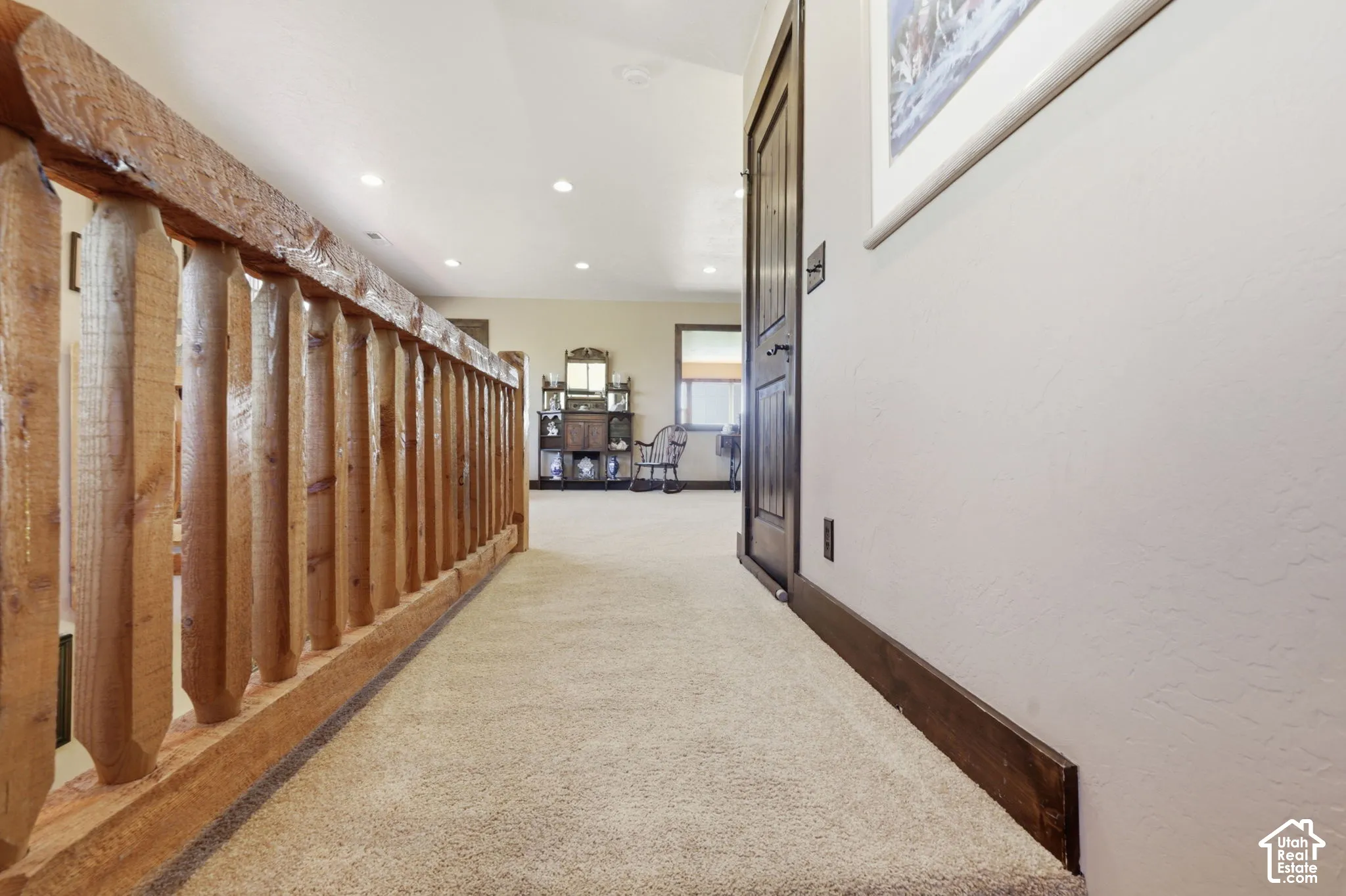 Hallway featuring custom log-style wooden handrails, recessed ceiling lighting, carpeted flooring, and dark-stained wooden door trim