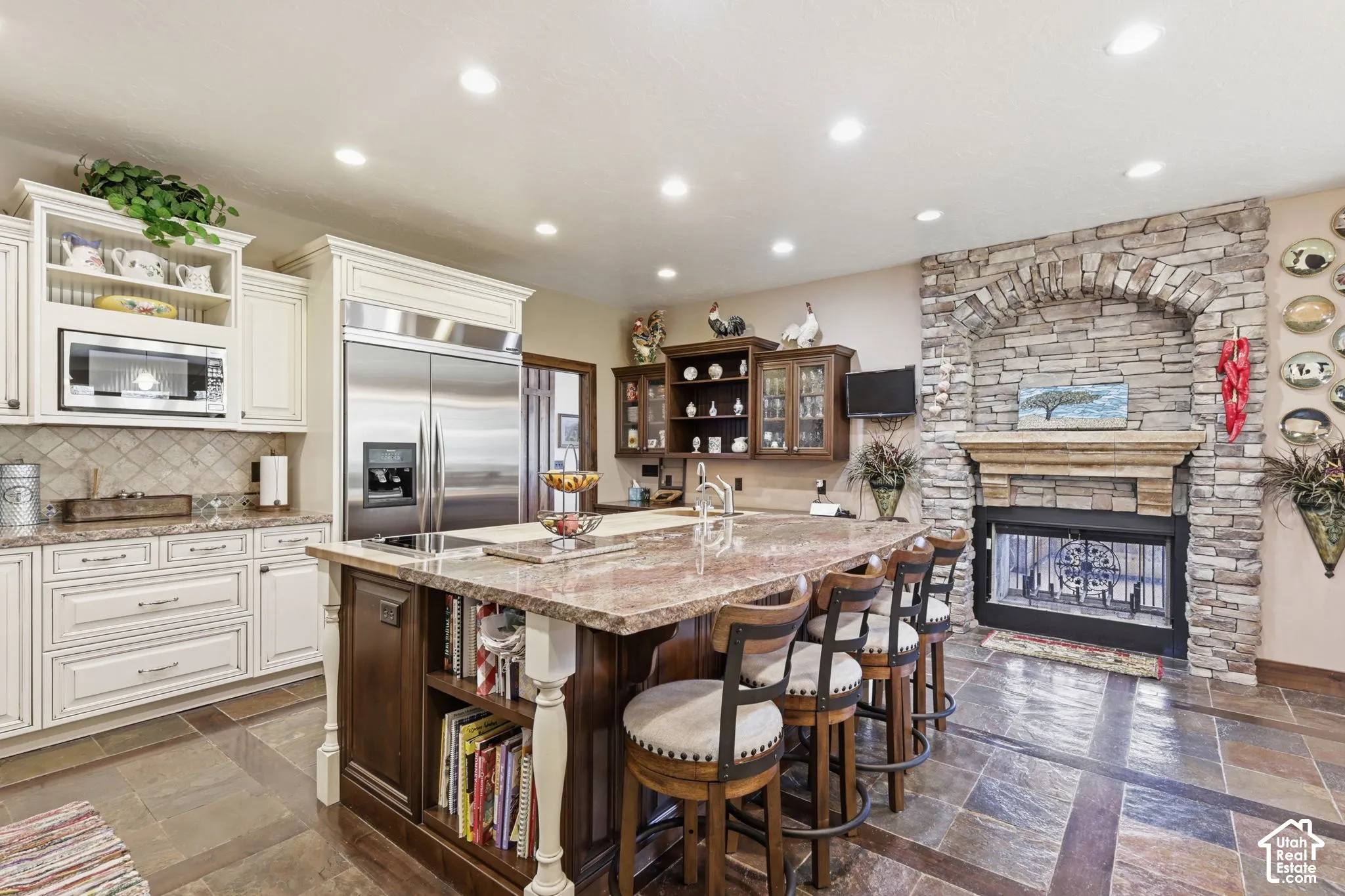 Kitchen featuring custom cabinetry, a stone-surround fireplace with a wooden mantel, a large central island with integrated storage, stainless steel appliances, and tile flooring