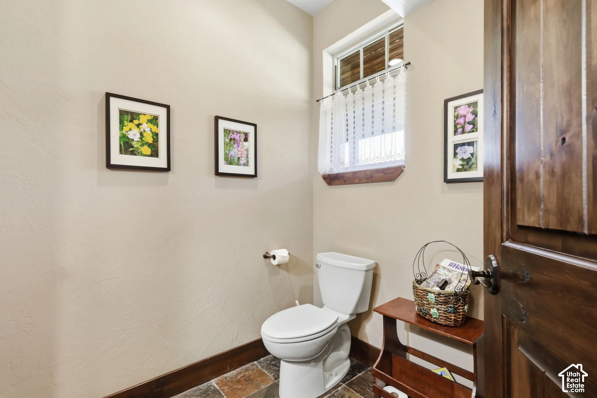 Powder room featuring multi-tonal stone tile flooring, stained wood door with iron hardware, and a single-hung window with a wood sill