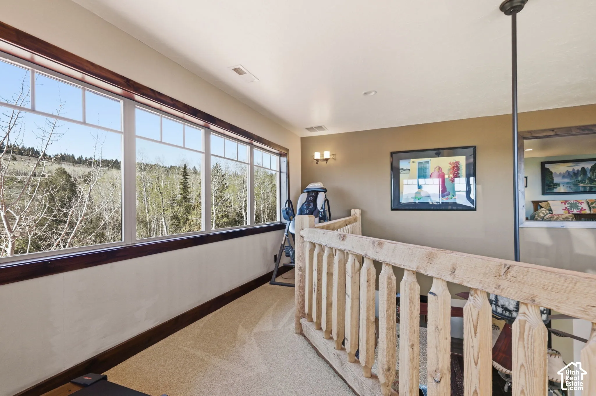 Expansive wall of windows with dark wood trim, natural wood balustrade railing, wall-mounted light fixture, and neutral carpeting