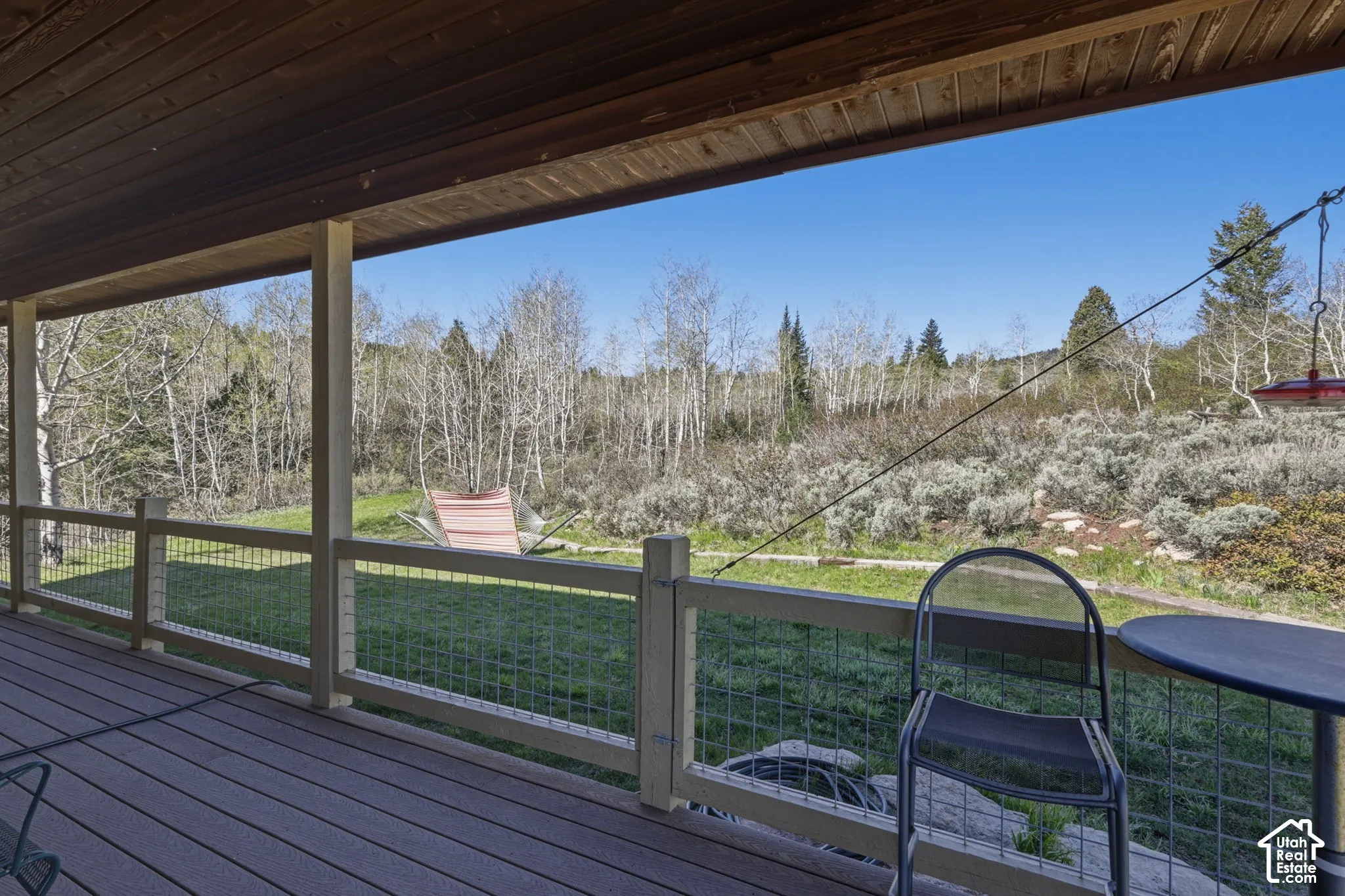 Covered wooden deck featuring a ceiling with exposed wood-finish beams, integrated support posts, and a railing system with wire mesh paneling