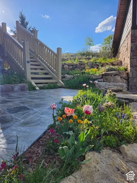 Stone patio featuring stacked stone retaining walls, landscape plantings, and wooden staircase with railings