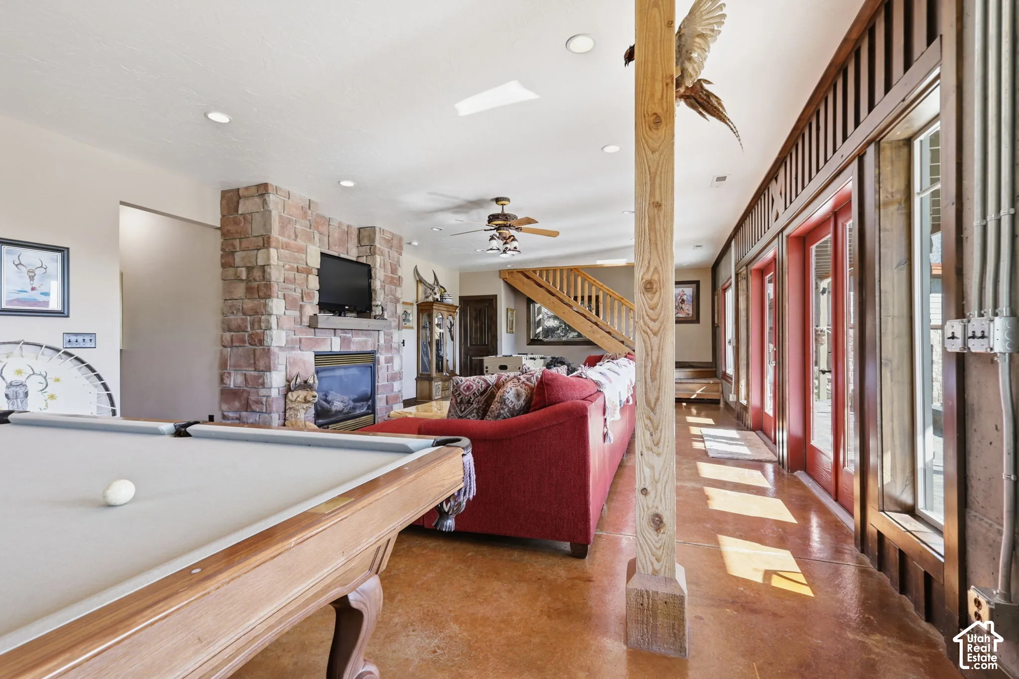 Interior space featuring natural stone fireplace surround, stained concrete flooring, exposed wood support pillar, recessed lighting, and multiple full-length glass panel doors