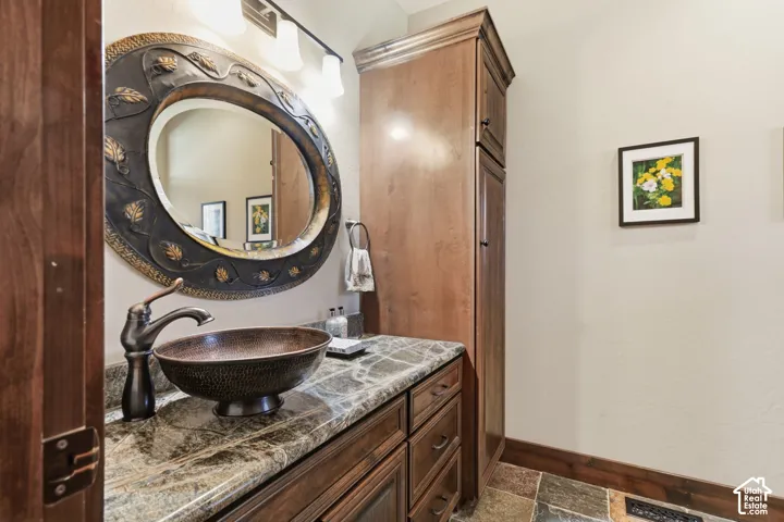 Custom wood-finish vanity featuring stone-finish countertop, hammered copper vessel sink, ornate oval mirror, and tall integrated cabinetry