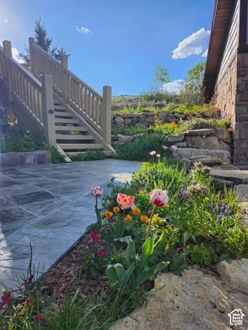 Stone patio featuring stacked stone retaining walls, landscape plantings, and wooden staircase with railings