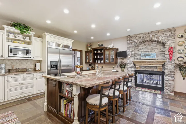 Kitchen featuring custom cabinetry, a stone-surround fireplace with a wooden mantel, a large central island with integrated storage, stainless steel appliances, and tile flooring