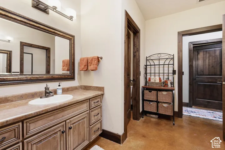 Stained wood cabinetry with an integrated countertop, oval drop-in sink, framed vanity mirror, three-light fixture, and polished concrete flooring