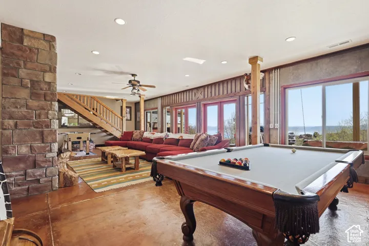 Full-height stone chimney, recessed lighting, wood-post structural elements, stained concrete flooring, and multi-panel glass doors