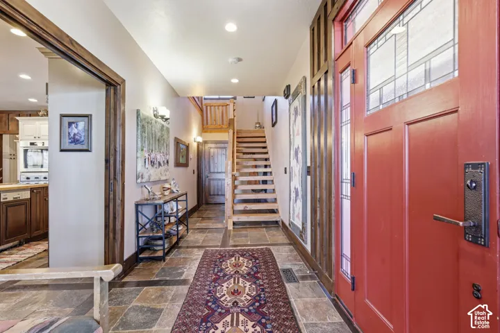 Entryway featuring a red stained-wood door with leaded glass accents, natural stone tile flooring, an open-tread wood staircase, and wood-trimmed archways
