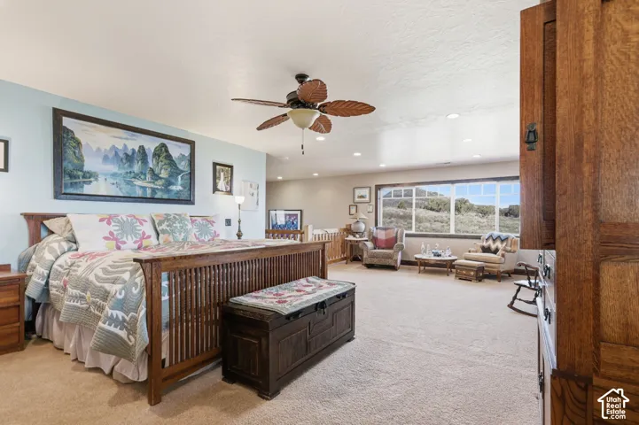 Spacious room featuring neutral carpeting, recessed lighting, a ceiling fan with leaf-motif blades, and a large multi-pane window with a natural landscape backdrop