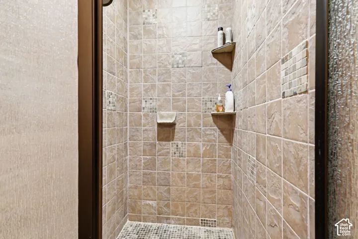 Walk-in shower featuring textured ceramic wall tiling, glass mosaic accent insets, integrated corner shelving, and a mosaic-tile floor
