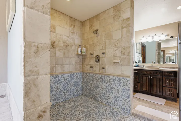 Shower enclosure featuring natural stone tile wall surrounds, patterned ceramic floor tiling, multiple integrated shower heads, and a dark wood-finish vanity with a vessel sink