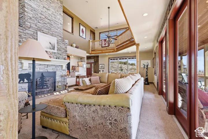 Floor-to-ceiling stone fireplace, high vaulted ceilings, expansive glass sliding doors, elevated wooden balcony with railing, and recessed lighting