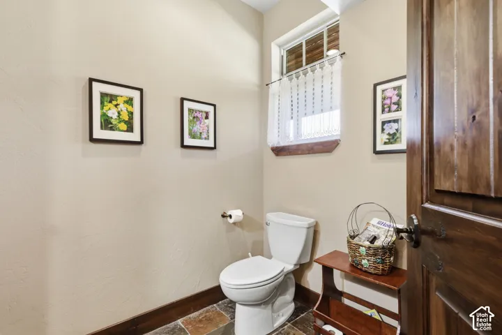 Powder room featuring multi-tonal stone tile flooring, stained wood door with iron hardware, and a single-hung window with a wood sill