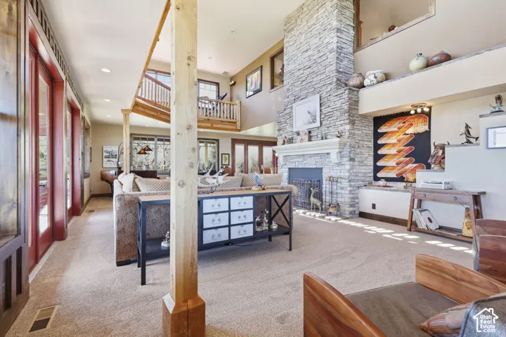 Full-height stone fireplace with a prominent mantel, architectural exposed timber support posts, elevated wooden mezzanine with spindle railing, and floor-to-ceiling glass panel doors