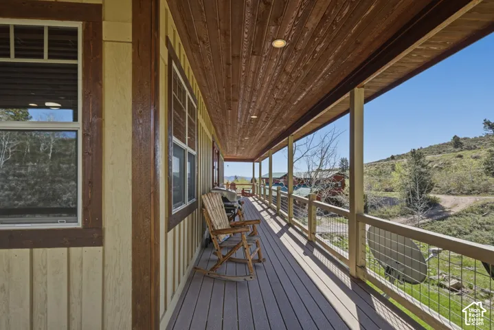 Covered wrap-around deck featuring a stained wood-plank ceiling, recessed lighting, composite decking, and a metal cable railing system