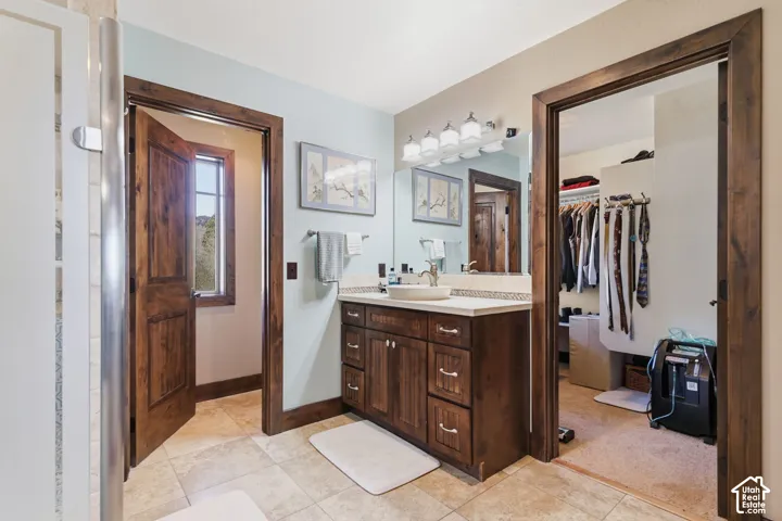 Bathroom featuring a wood vanity cabinet with a vessel sink, stone-finish tile flooring, large wall-mounted mirror, and multi-bulb vanity lighting
