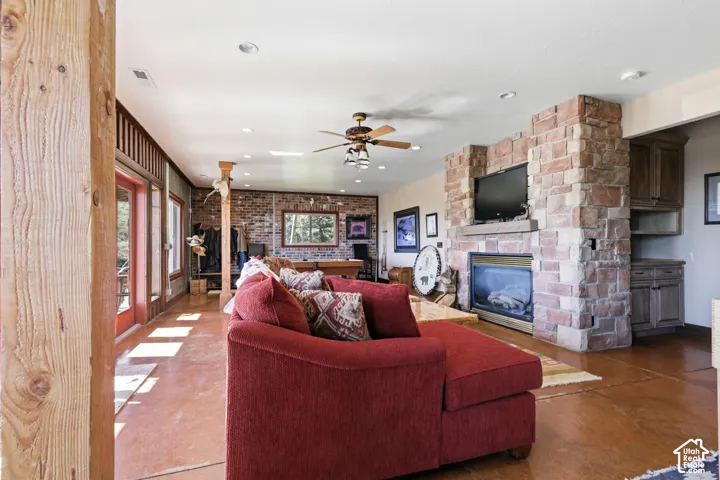 Living area featuring a floor-to-ceiling stone fireplace, exposed brick walls, stained concrete flooring, recessed lighting, and timber support posts