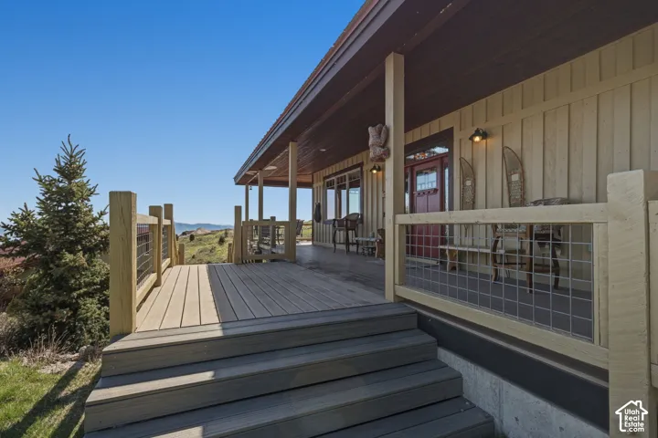 Covered wrap-around deck featuring synthetic decking, metal grid railings, vertical siding, and exterior wall-mounted lighting