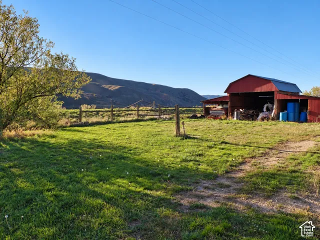 Open pasture land with split-rail fencing, a red metal-sided barn, and mountainous terrain