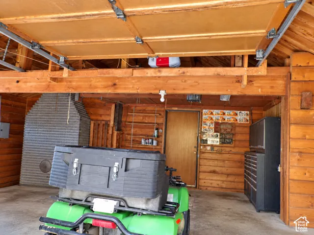 Garage interior featuring exposed timber log walls, a structural overhead wooden beam, a concrete floor, built-in metal cabinetry, and mounted wall shelving