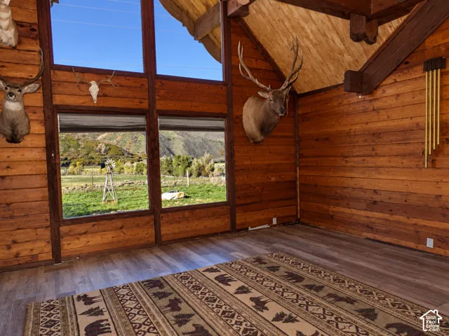 Vaulted ceiling featuring exposed timber beams, wood-plank wall paneling, large multi-pane windows, and wood-finish flooring