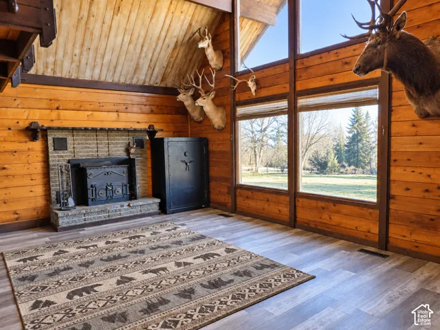 Vaulted wood-paneled ceiling, floor-to-ceiling windows, wood-finish flooring, and a stone-surround fireplace with an iron wood-burning stove insert