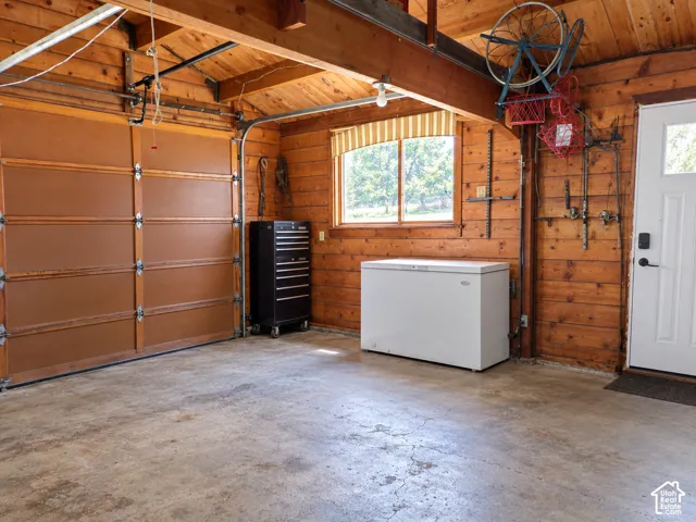 Garage featuring horizontal wood wall paneling, exposed structural timber beams, concrete flooring, and a multi-panel overhead garage door
