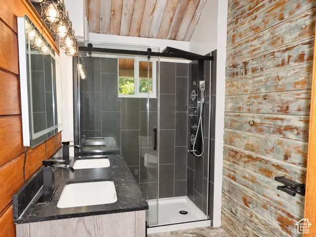 Double vanity featuring a dark stone-finish countertop, dual white rectangular undermount sinks, matte black fixtures, and a lighted rectangular mirror