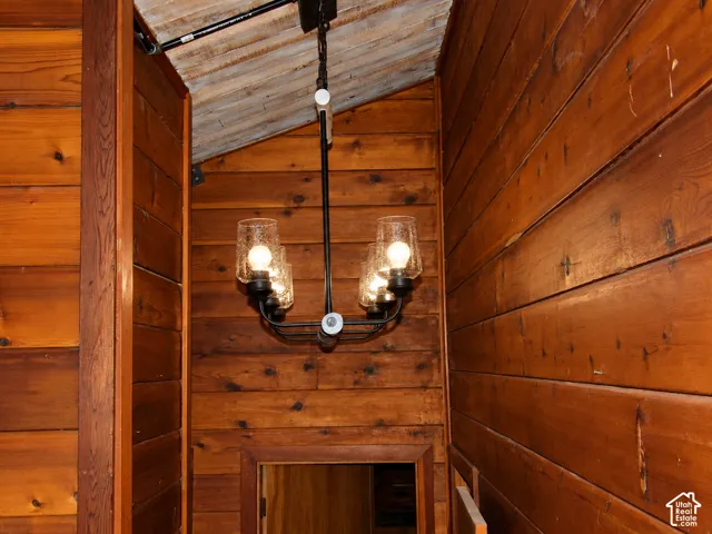 Horizontal wood plank wall paneling, vaulted ceiling with exposed wood beams, and a six-light chandelier featuring matte black finish and seeded glass shades