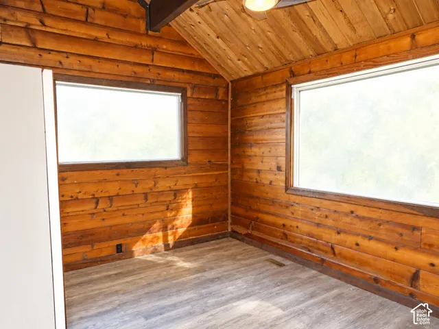 Interior room featuring tongue-and-groove log wall paneling, vaulted ceiling with exposed wooden beam, two windows, and wood-finish flooring