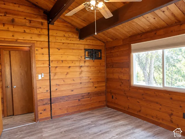 Interior space featuring tongue-and-groove wood wall paneling, vaulted ceiling with exposed structural beams, wood-finish flooring, and ceiling fan with integrated lighting