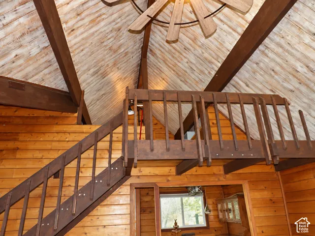 Vaulted ceilings with exposed timber beams, whitewashed wood plank ceiling detail, interior wood paneling, and an open timber staircase with matching wooden railings