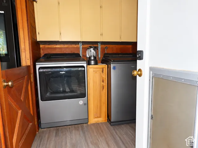 Laundry area featuring wood-finish flooring, upper wall-mounted cabinetry, a built-in narrow cabinet, and wood-paneled wall accents
