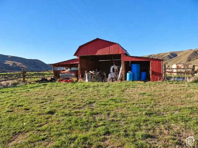 Red metal-sided barn featuring open-bay storage and split-rail fencing, situated on expansive acreage with a mountain backdrop