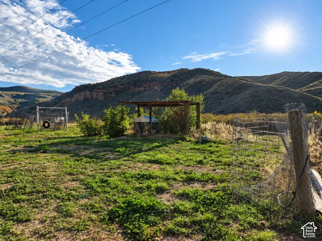 Expansive outdoor area featuring a wooden pergola, wire fencing, mature vegetation, and a prominent mountain backdrop